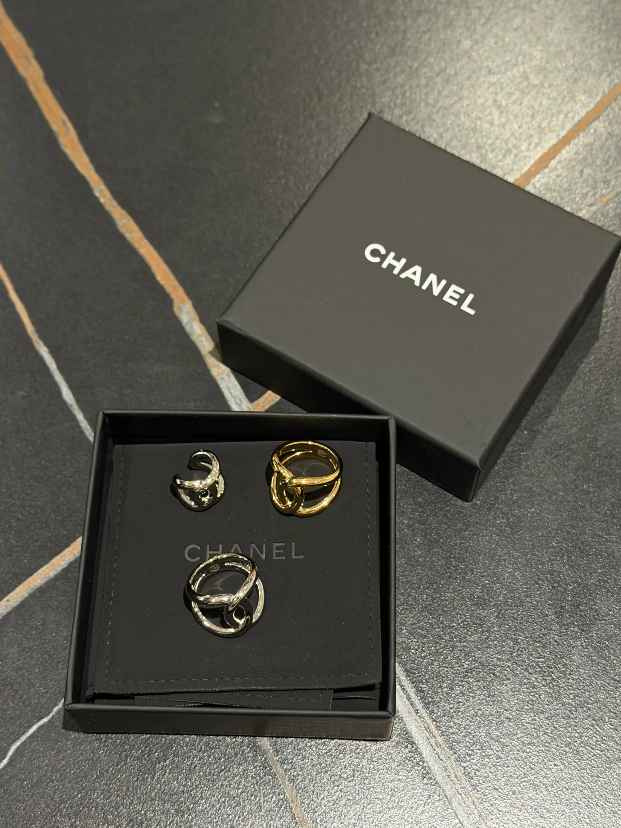 CHANEL Fall-Winter 2026(2026秋冬系列)雙C配飾實物,分別為金色及銀色雙C戒指,左上方可見同系列銀色耳夾;戒指及耳夾均以交疊雙C設計作為主要視覺元素。