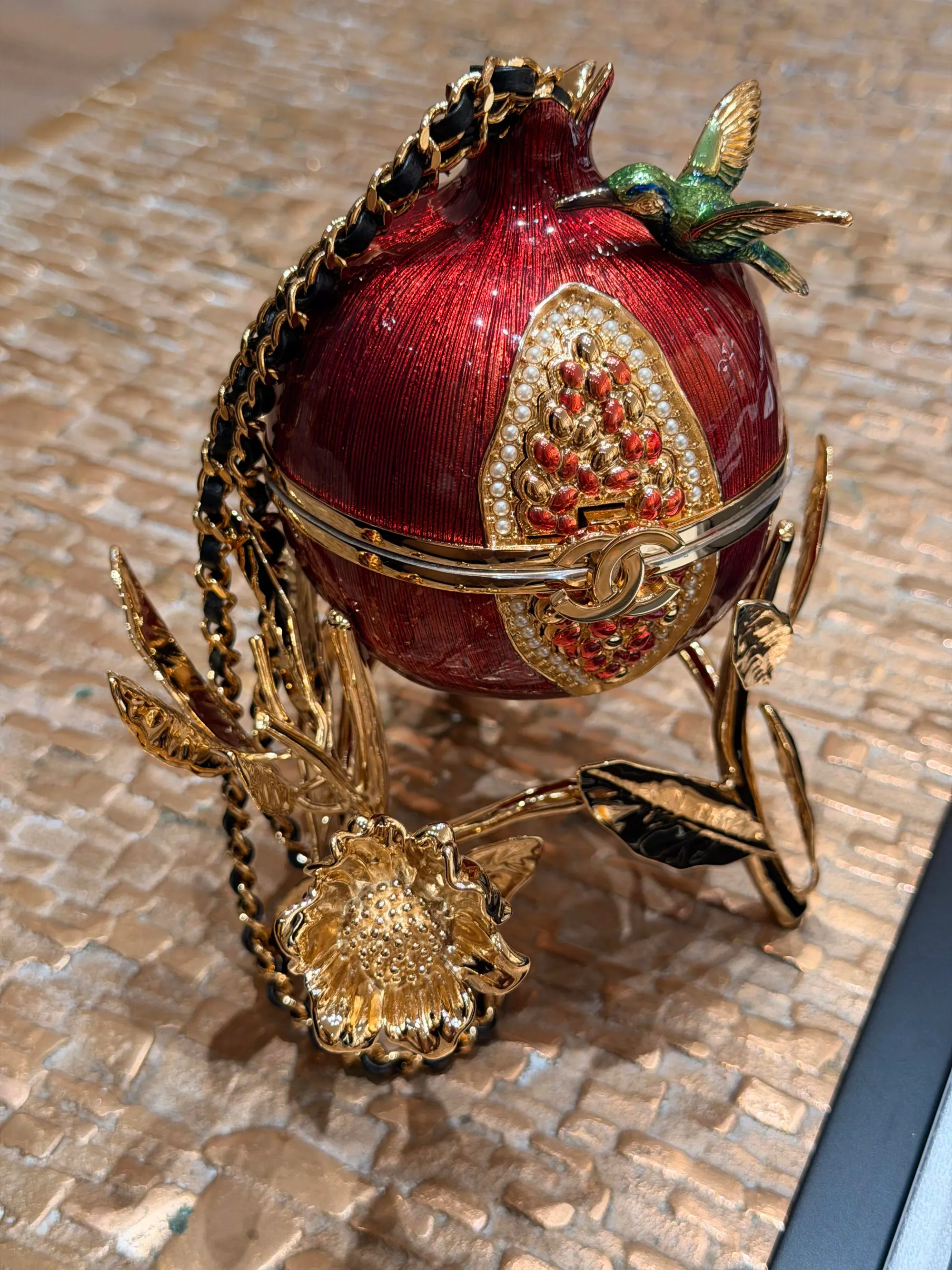 石榴造型晚宴包以紅色琺瑯及金屬細節呈現果實外形，立體輪廓成為作品嘅主要視覺特色。