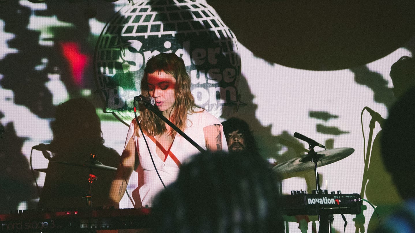 Woman plays keyboard and sings into a mic while drummer sits at drum kit behind her