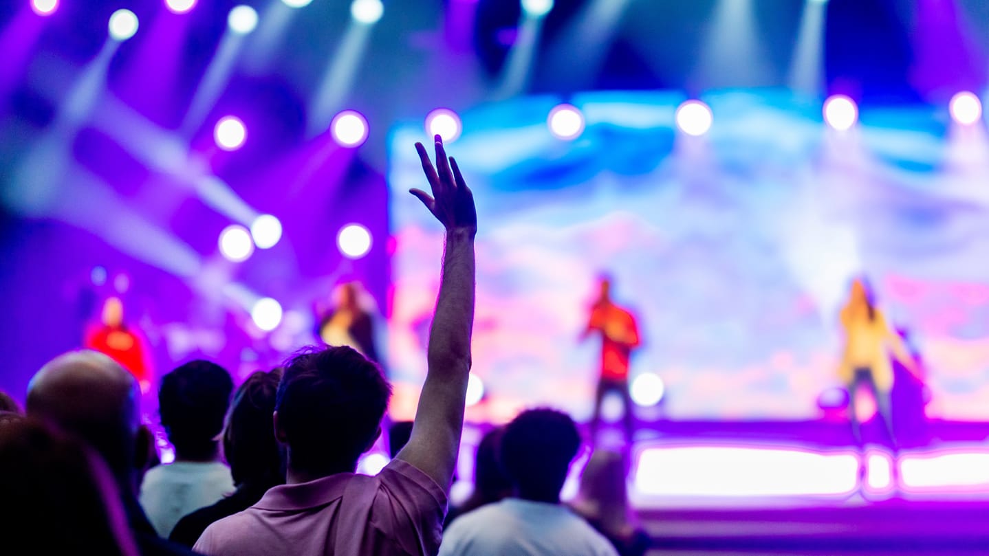 Audience member stands holding up their hand in a crowd at a stage.
