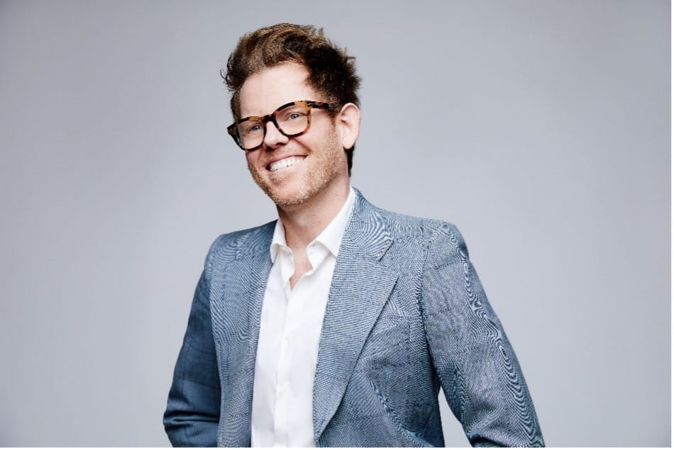 Smiling man with glasses wearing a white shirt against a grey background