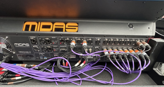 A screen grab of a midas HD96 console rear panel is depicted with purple cables and an orange logo that written "midas" on a black background