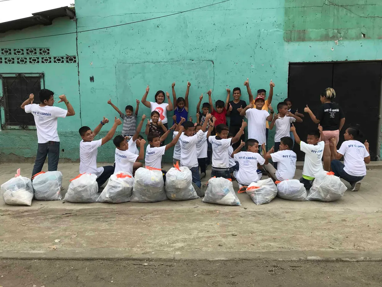 Children participating in a community cleanup activity, wearing matching "soy el cambio" t-shirts, with bags of collected tra