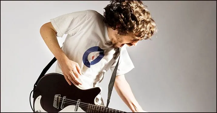 Guitarist playing guitar passionately, wearing a white t-shirt with a logo, engaging in music performance or practice.