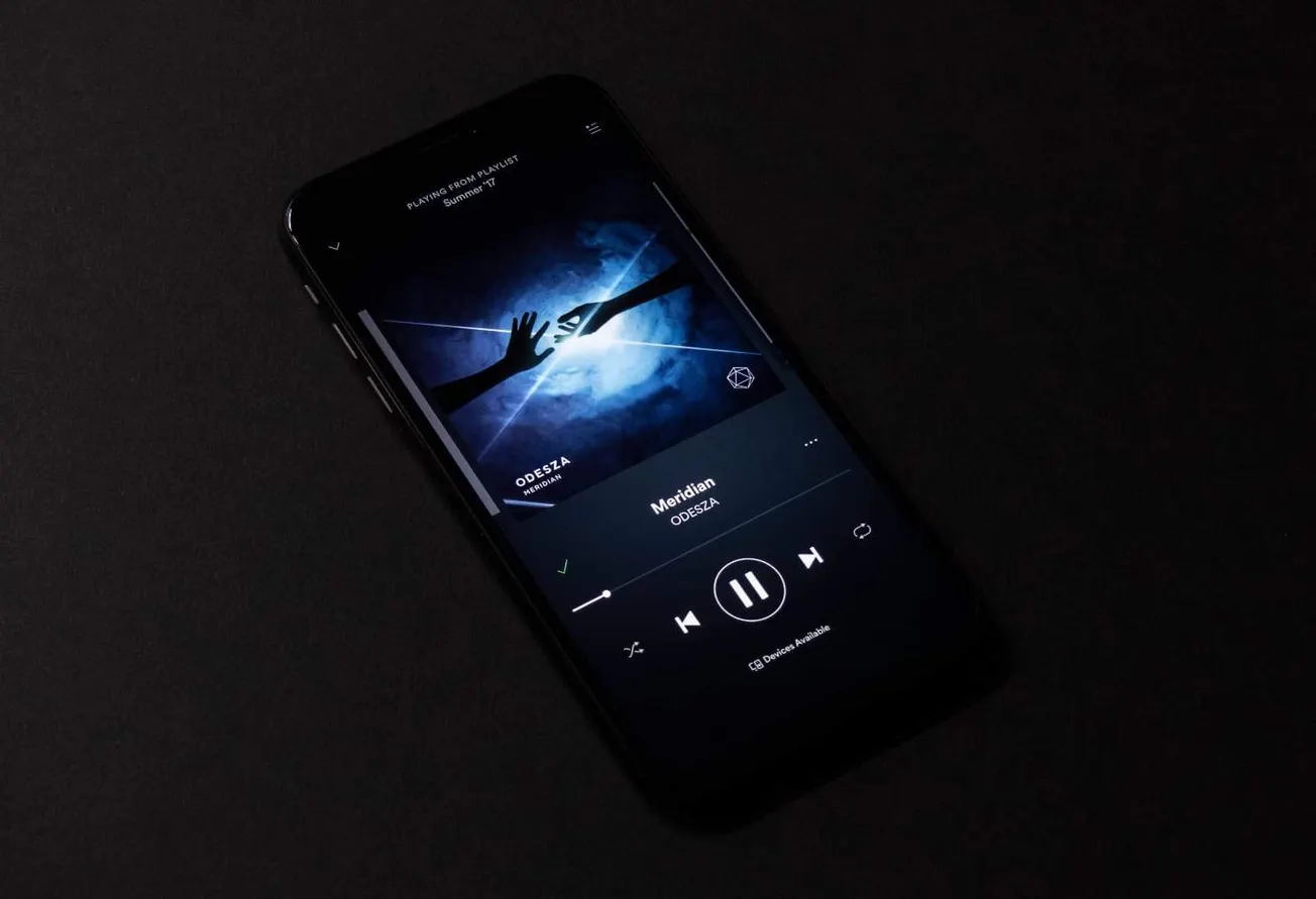Music streaming app on smartphone displaying song "Meridian" by ODESZA in dark setting.