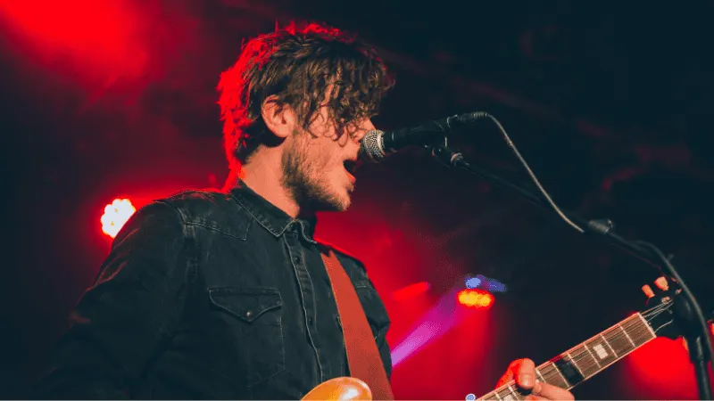 Soft-focus photo of a young male musician playing an electric guitar and singing into a microphone on stage with vibrant red
