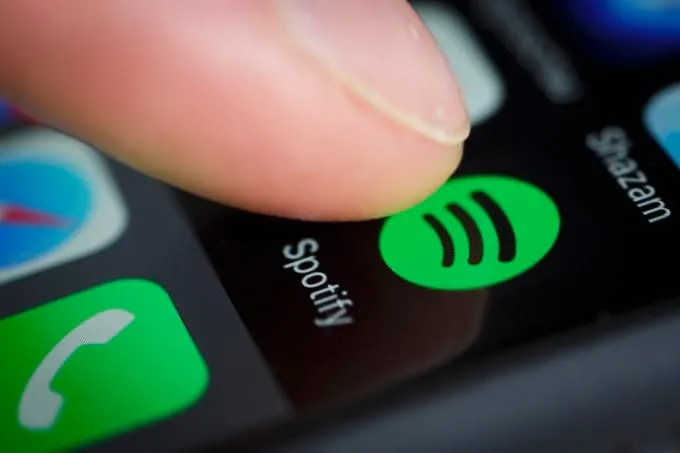 Spotify app icon on a smartphone screen, close-up of a finger pressing the green Spotify logo, representing music streaming,