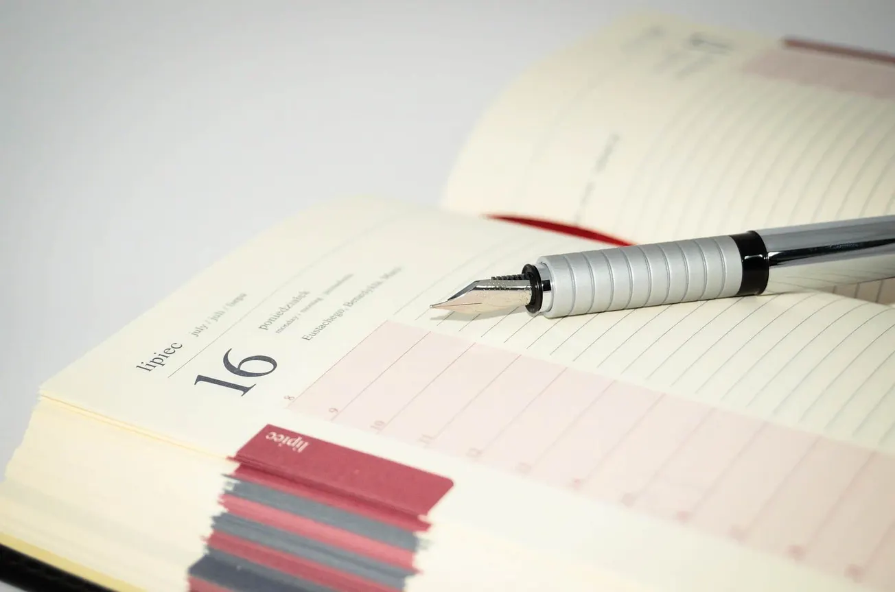A silver fountain pen resting on an open planner with dated pages, highlighting organization and scheduling tools.