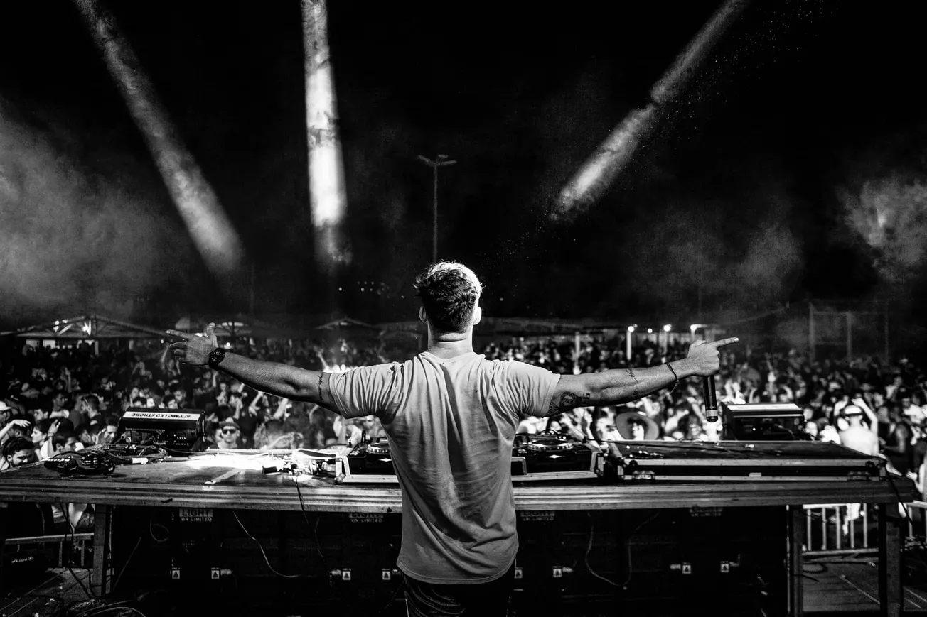 DJ performing at a lively music festival with a large crowd, stage lighting, and energetic atmosphere enhancement.