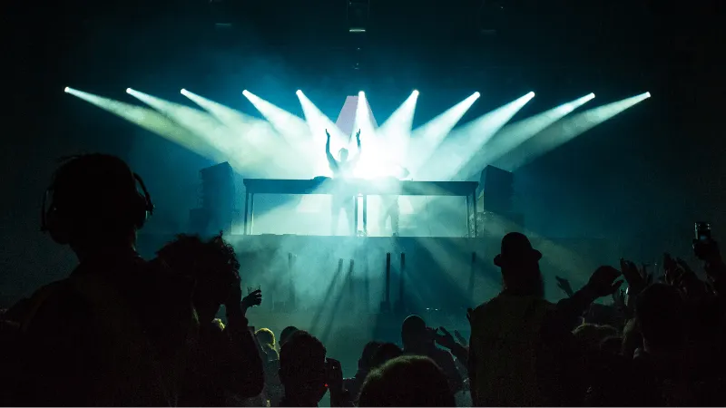 DJ performing at a concert with vibrant stage lighting and a lively audience, capturing the energy and excitement of a live m
