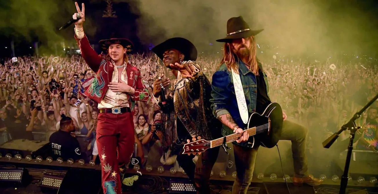 Bright concert performers wearing cowboy hats and colorful outfits on stage with a lively crowd audience in the background ca