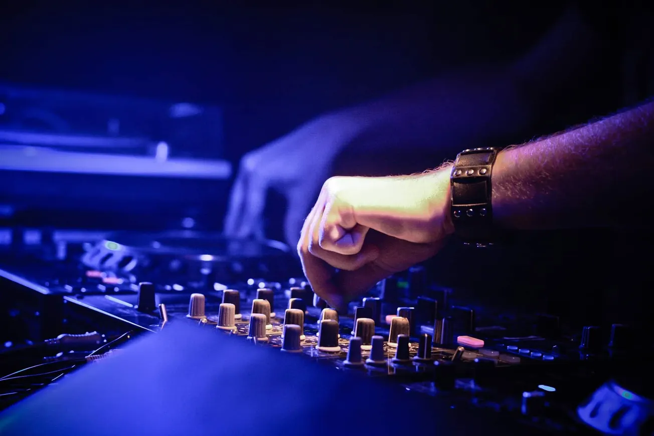 High-tech DJ mixing console at a music event showing hands adjusting sound equipment with vibrant lighting.