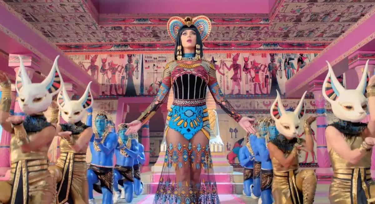 Egyptian goddess cosplay with elaborate costume and staff surrounded by dancers with white animal masks in colorful Egyptian-