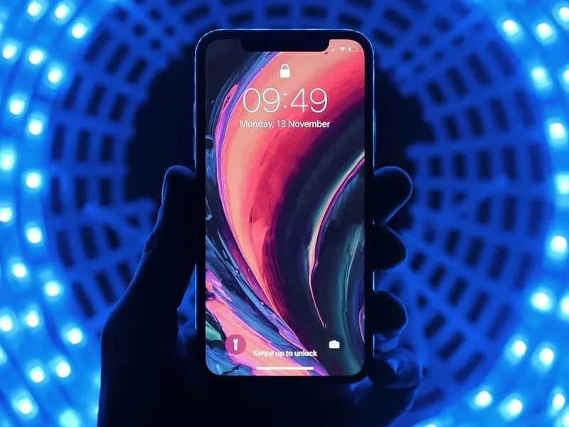 Smartphone with vibrant abstract wallpaper, illuminated by glowing blue LED lights in the background, showcasing modern mobil