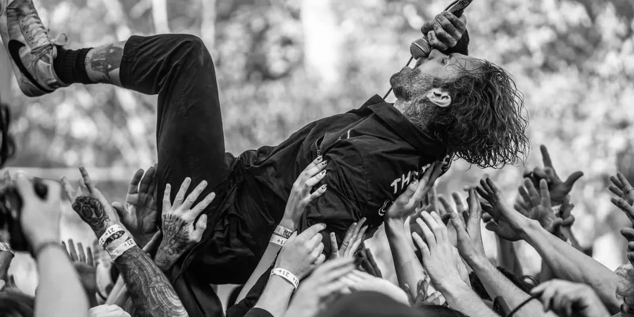 A dynamic black and white image of a rock singer crowd surfing during a live concert, surrounded by enthusiastic fans reachin