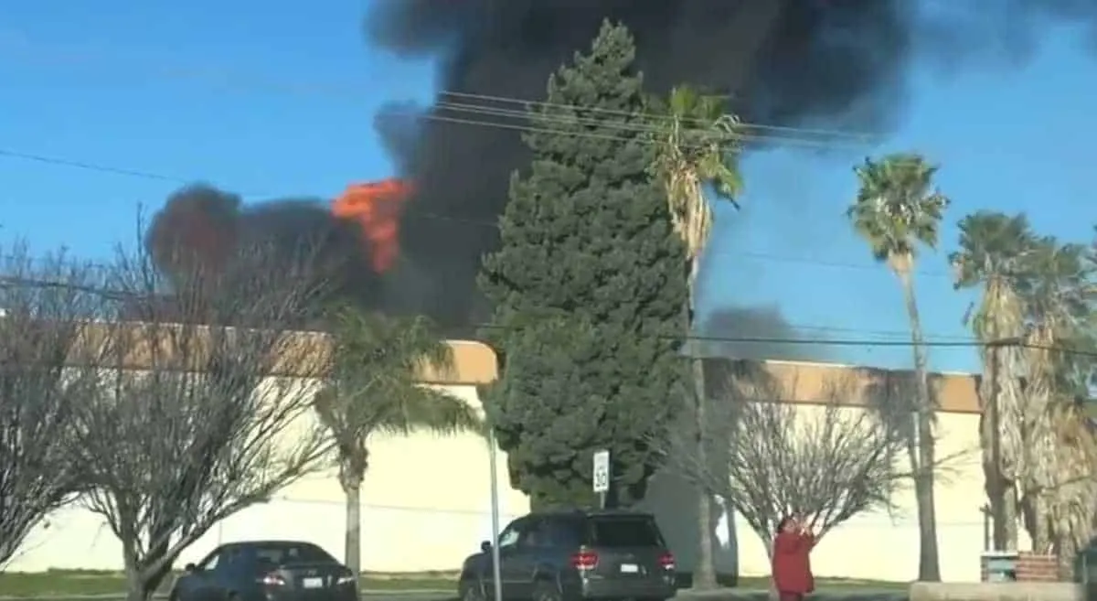 Fire emergency wildfire burning in urban area with thick black smoke and flames behind trees and building, emergency response