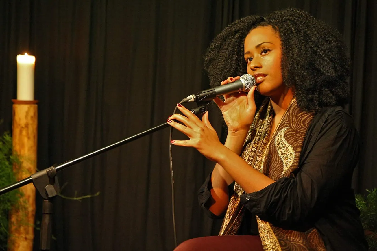 Vibrant Black woman singer performing on stage with microphone, cozy ambiance, candlelight, and dark backdrop blending with t