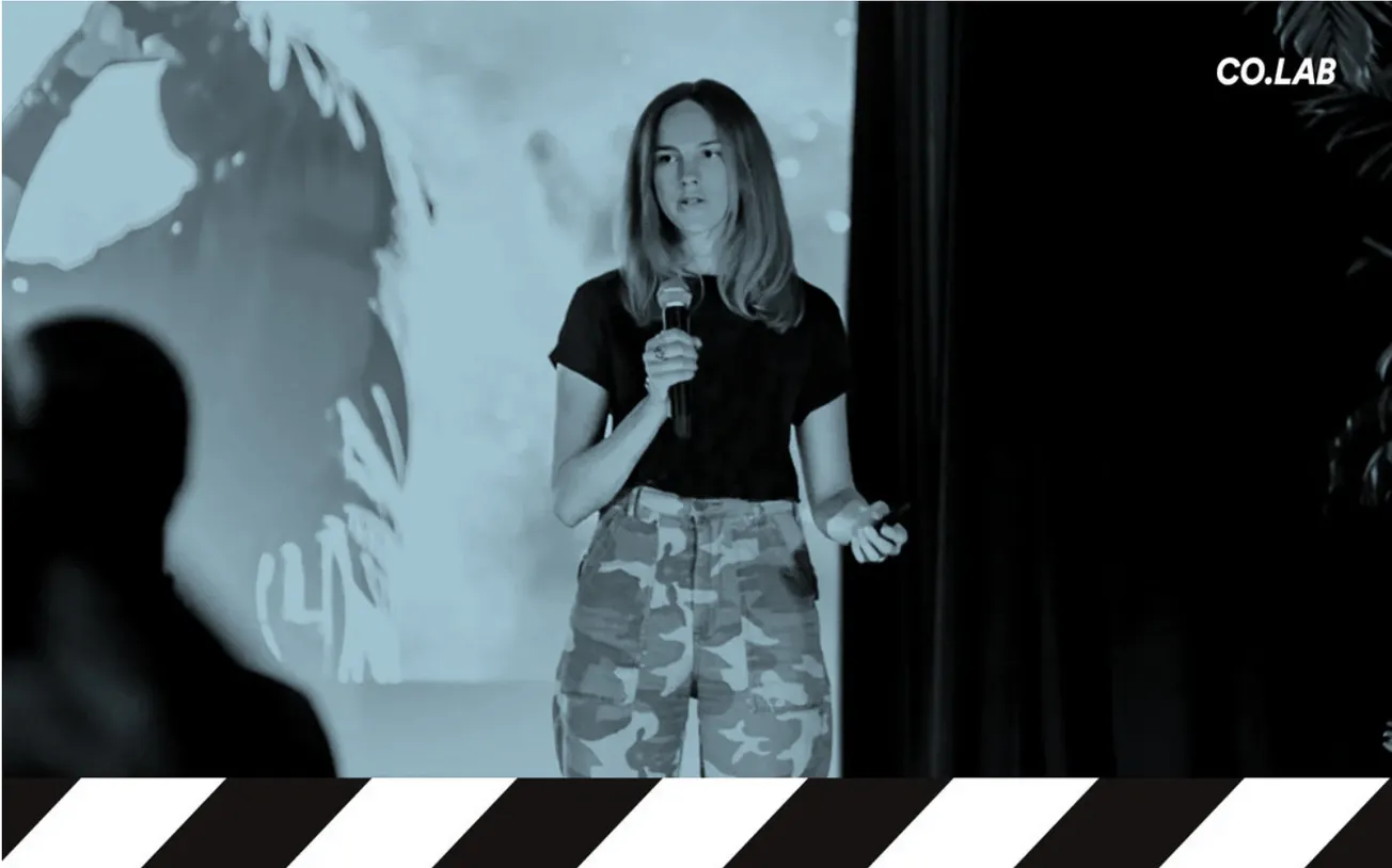 Woman giving presentation at tech conference or workshop, young female speaker with microphone, casual clothing, urban enviro