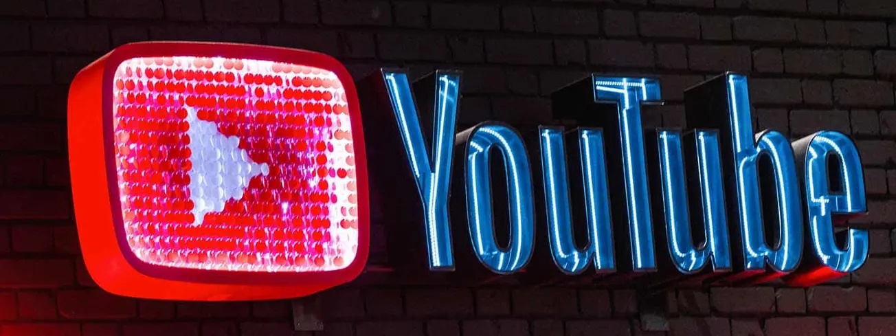 Red and blue neon YouTube logo sign with brick wall background, popular for digital content, social media branding, and onlin