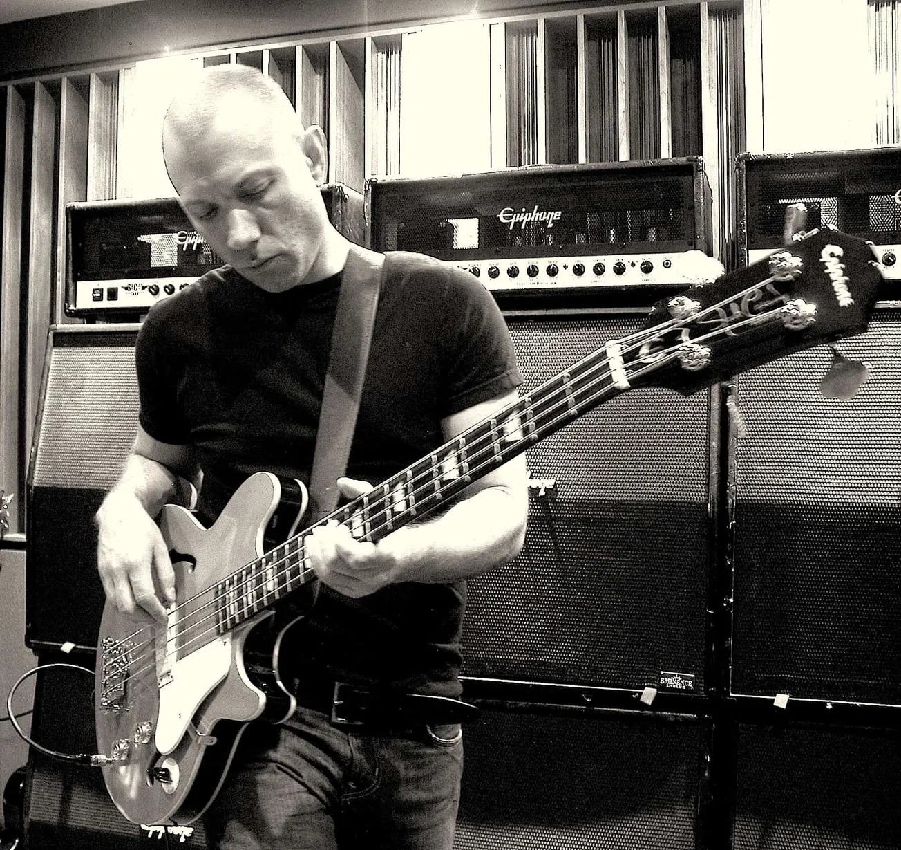 Playing electric bass guitar in a music studio with amplifiers in the background, black and white photo capturing a musician