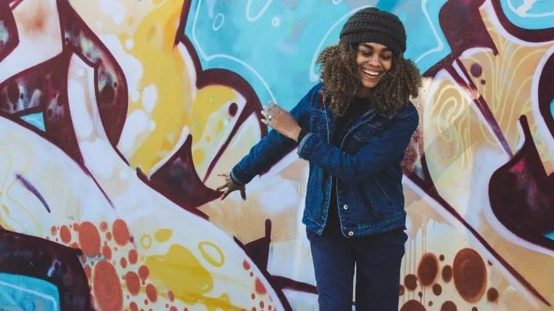 Colorful graffiti wall with smiling young woman enjoying urban street art, showcasing creativity and modern culture.