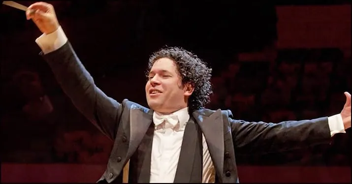 Conductor leading an orchestra, passionately conducting with arms outstretched in a concert hall setting.