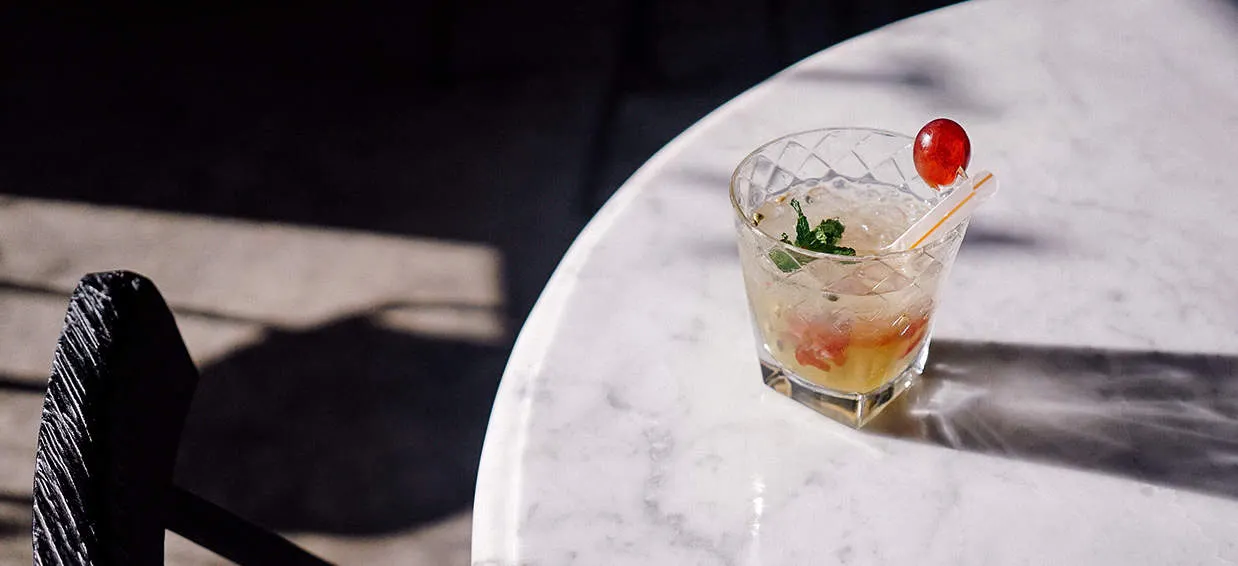 Refreshing cocktail with mint and cherry in a crystal glass on a white marble table, perfect for beverage and drinks industry
