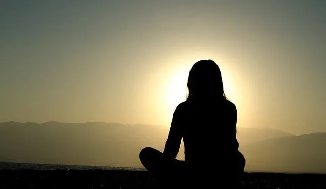 Woman practicing meditation at sunset for mindfulness and relaxation in nature.