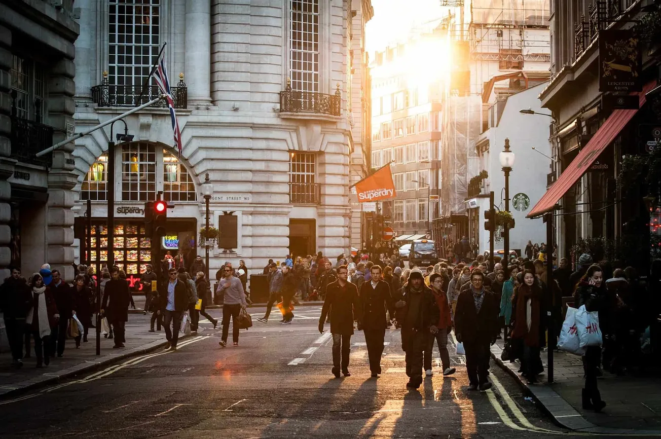 Busy city street in London during sunset, featuring historic architecture, pedestrians crossing, and vibrant urban life.