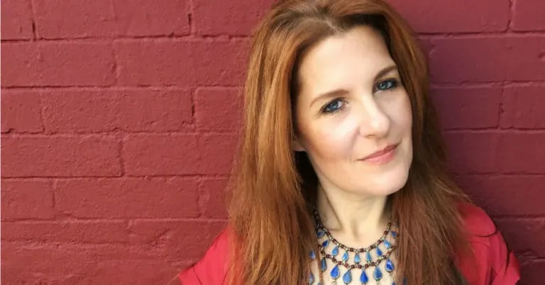 Independent woman with red hair in front of red brick wall, confident and professional, wearing a statement necklace and red