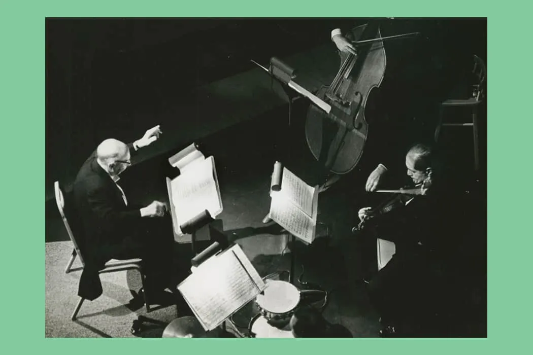 Elderly classical musicians performing a duet with a piano and violin on stage during a concert.