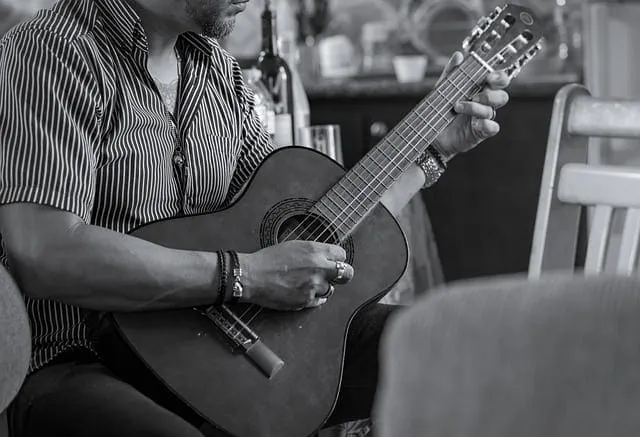 Guitarist playing acoustic guitar in home setting, casual music practice, musician hobby, indoor music session, Hypebot music