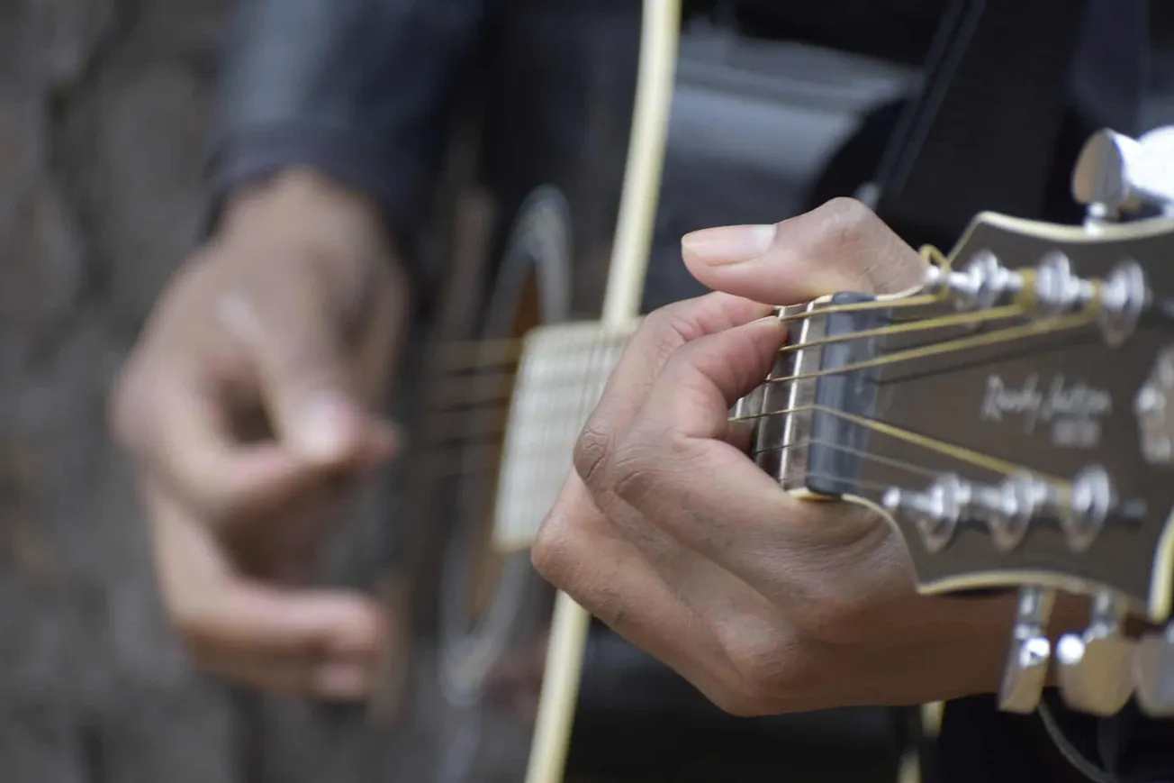 Acoustic guitar player hand close-up, focusing on fingers pressing strings on fretboard, live music performance, musician pla