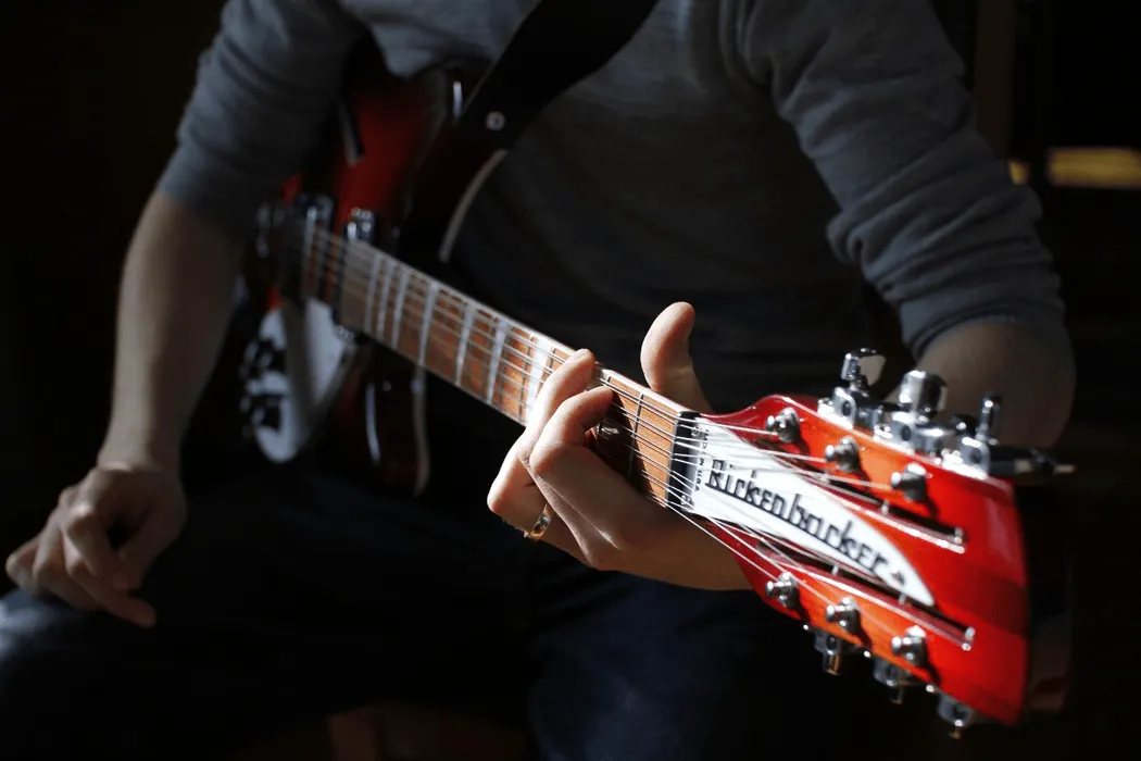 Guitarist playing an electric guitar, focusing on hand position on fretboard, with a Harkenbarker sticker on headstock, highl