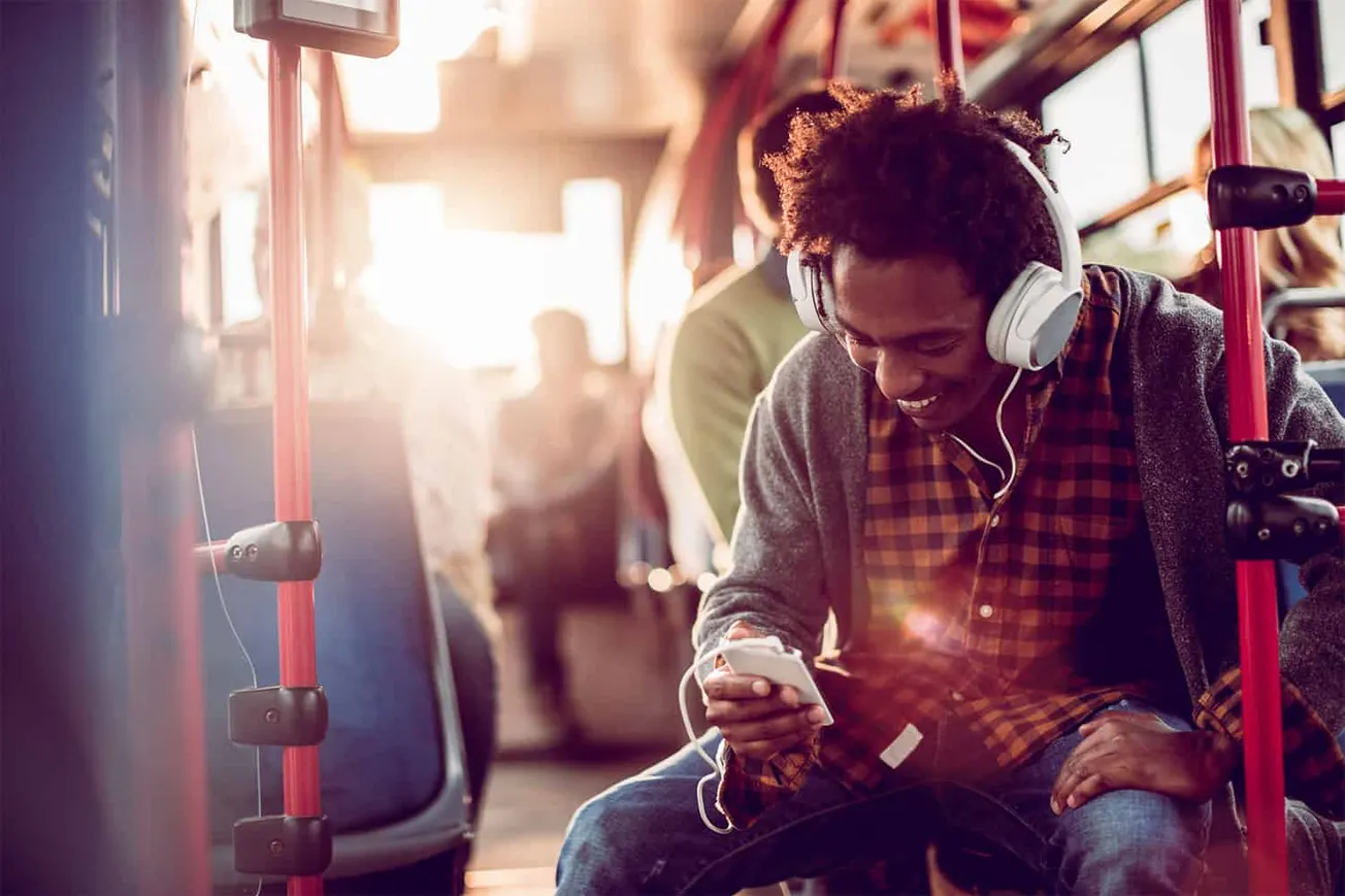 Young man with headphones using smartphone while sitting on a bus, enjoying music during commute, in urban transportation set