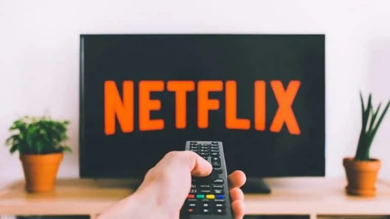 Netflix streaming on a TV screen with a hand holding a remote control, indoor setting with potted plants, emphasizing enterta