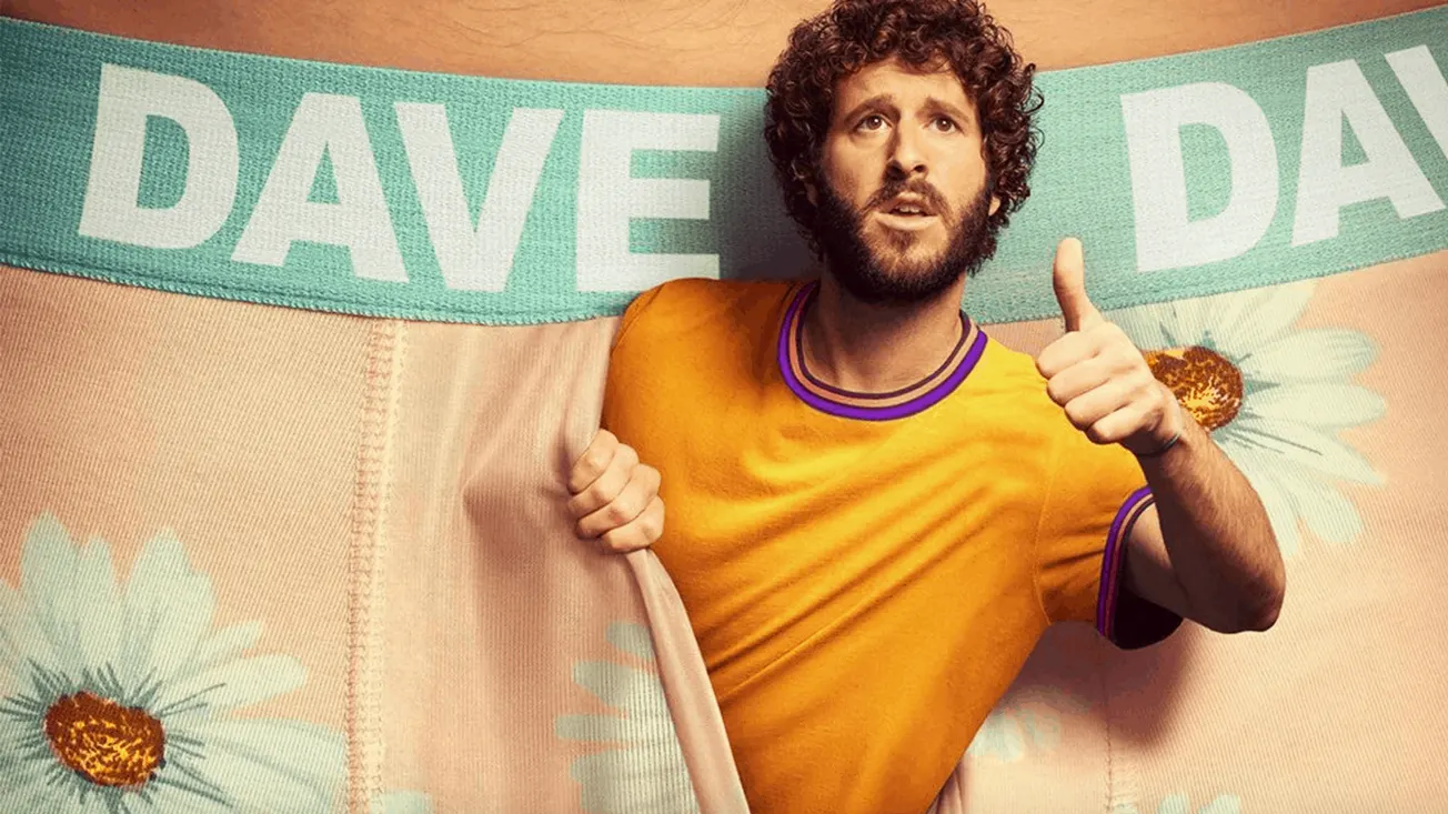 Bright yellow t-shirt, curly-haired man with beard, standing against colorful DAVE banner background, giving thumbs up, promo