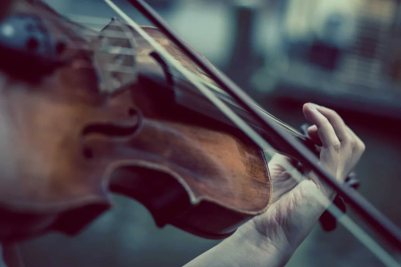 A person playing the violin with focus, capturing a close-up of the violin and hand on the instrument, highlighting musical a