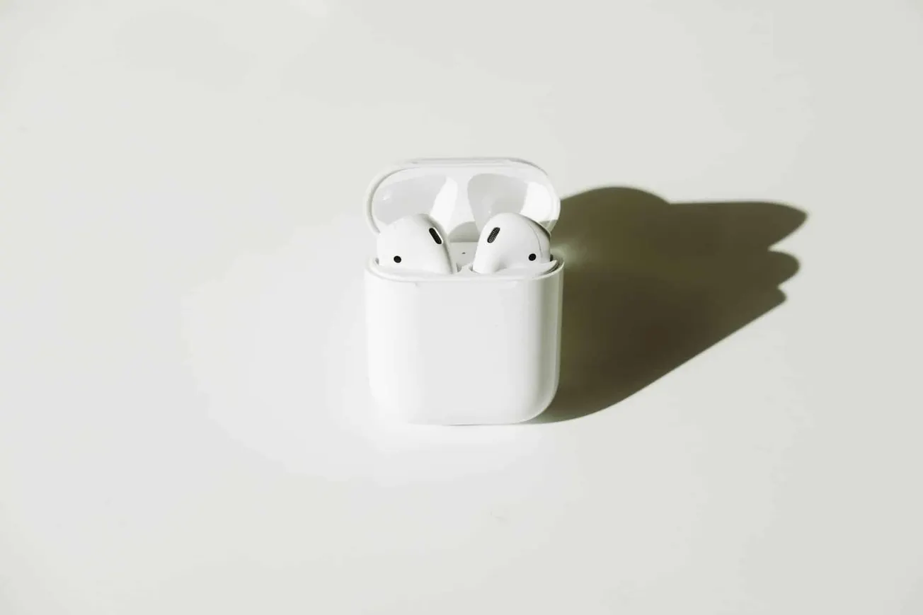 Wireless earbuds in their charging case on a plain surface with a sharp shadow, representing modern music technology and tren