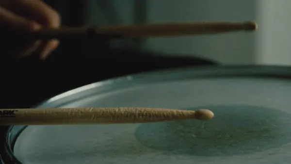 A close-up of drumsticks hitting a drumhead, emphasizing music performance and musician skill.