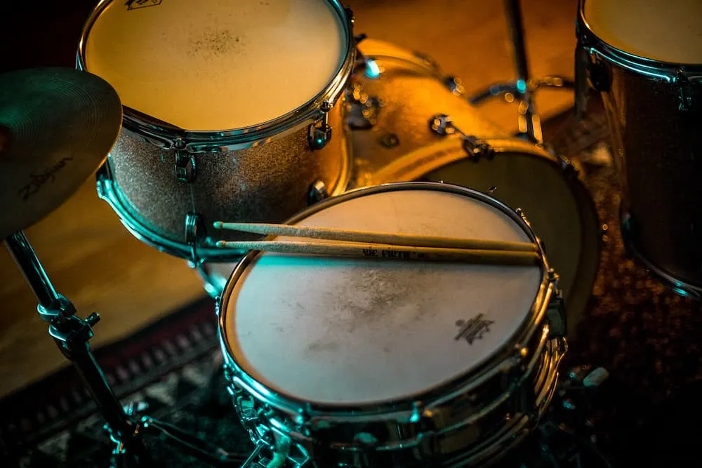 A drum set with cymbals and drumsticks on a textured surface in a cozy, dimly lit environment. Perfect for music enthusiasts,