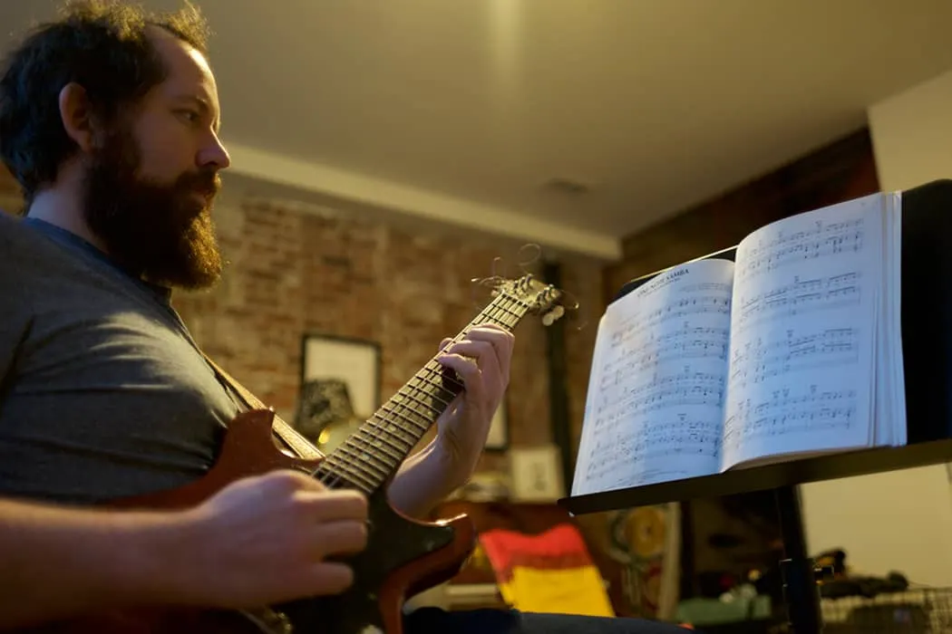 Guitarist practicing music at home, focused on sheet music, with a music stand, cozy indoor setting, featuring warm lighting