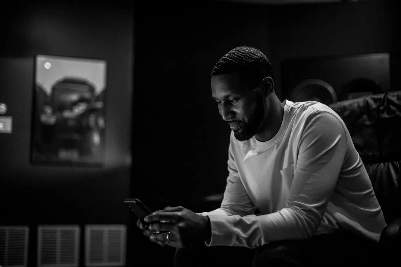 Young man using smartphone in music studio with professional audio equipment, black and white image.