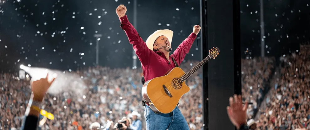 Live country music performance at a large outdoor concert with guitarist wearing a cowboy hat and raising arms in celebration