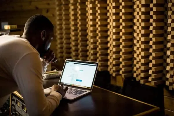 Laptop user working in a soundproof studio with acoustic foam panels for music or audio production.