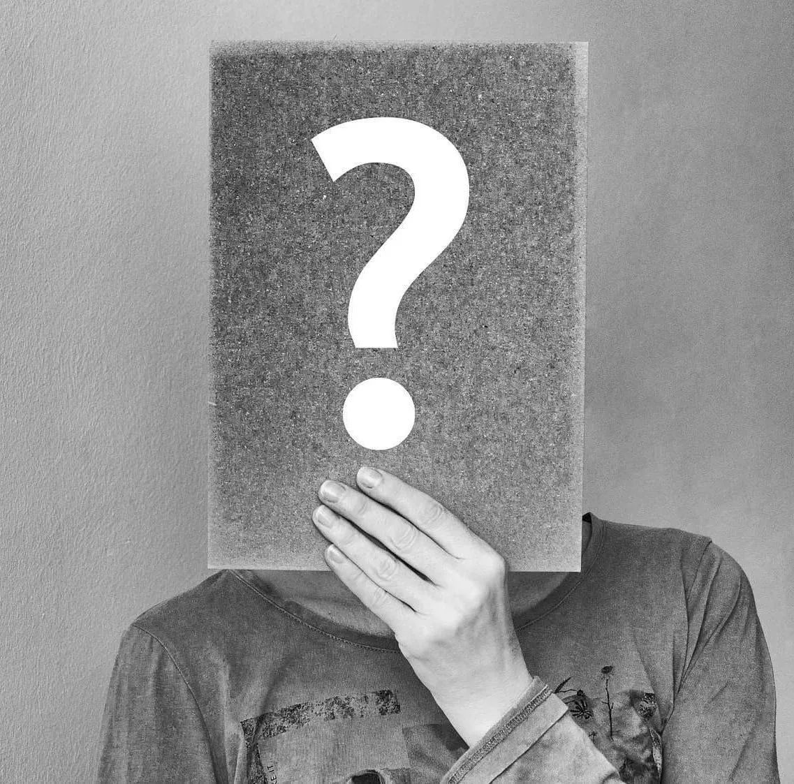 Mystery person holding a sign with a large white question mark, black and white image, concept of curiosity or unknown conten