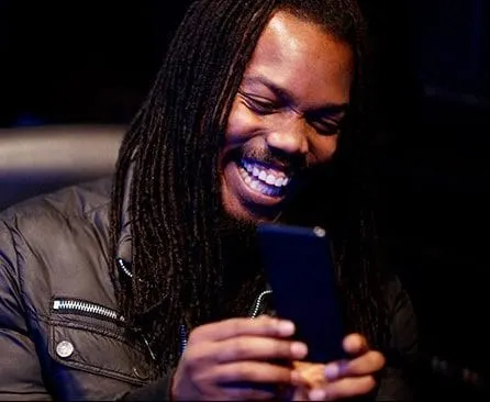Smiling man with dreadlocks using a smartphone at a music or tech event, showcasing digital engagement and modern communicati