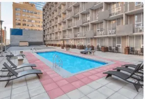 Poolside lounge chairs next to a rooftop swimming pool at a modern hotel or apartment complex. The image showcases relaxation