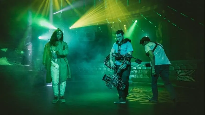Stylish woman and camera crew preparing for a music event with vibrant stage lighting in a nightclub or concert venue.