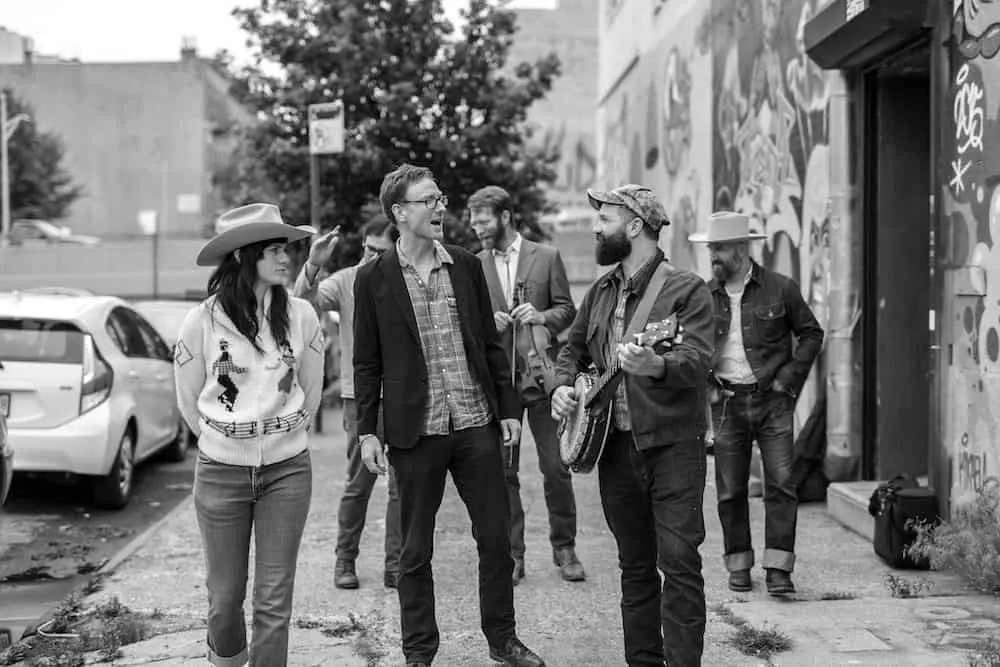 A group of young musicians and friends hanging out in an urban alleyway, with graffiti art on the walls, casually chatting, a